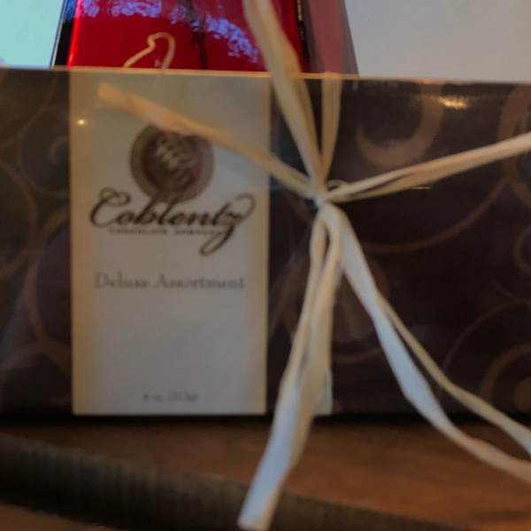 Wrapped gift box with a white ribbon and a red bottle behind it