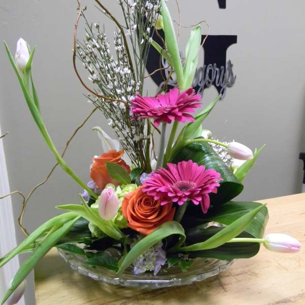 Mixed bouquet with pink gerberas, orange roses, and white tulips in a glass bowl