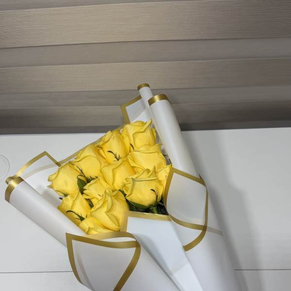 Bouquet of yellow roses wrapped in white paper with gold trim