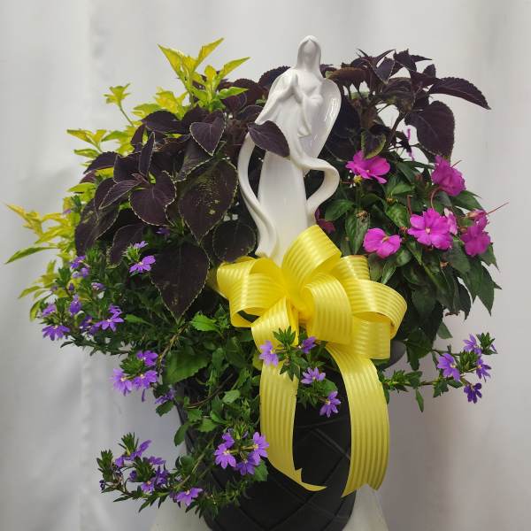 Potted mixed flowering plant arrangement with a white figurine and yellow ribbon