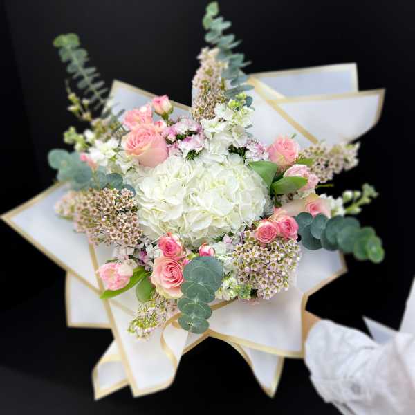 Bouquet of pink and white flowers wrapped in white paper with gold trim