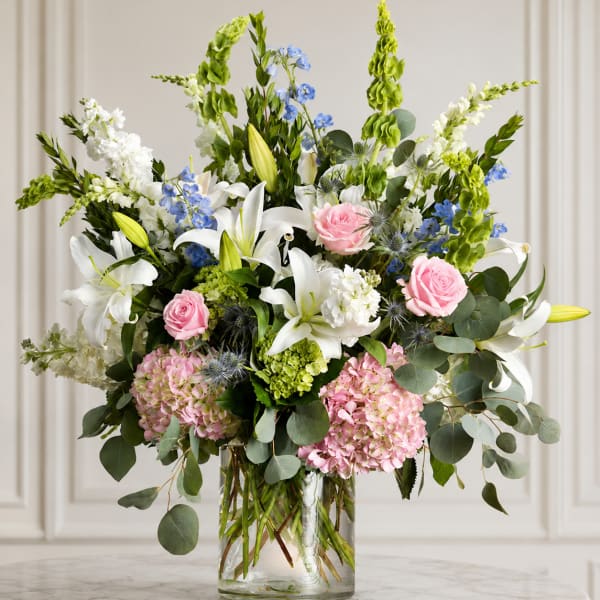 Mixed bouquet of white lilies, pink roses, and blue flowers in a glass vase