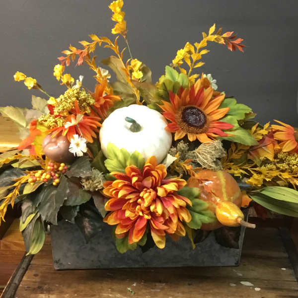 Autumn centerpiece with orange flowers, pumpkins, and a white gourd in a rectangular container