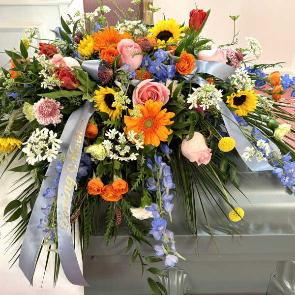 Large casket spray with mixed colorful flowers and blue ribbons