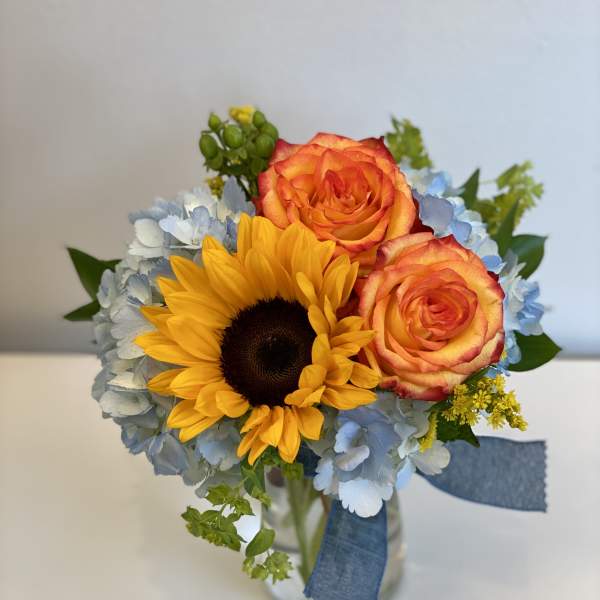 Bouquet of sunflowers, orange roses, and blue hydrangeas in a glass vase