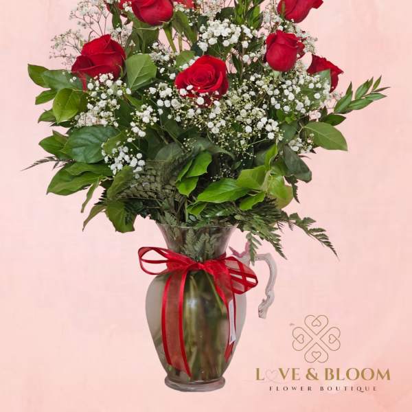 Red roses arranged in a glass pitcher with baby's breath and greenery
