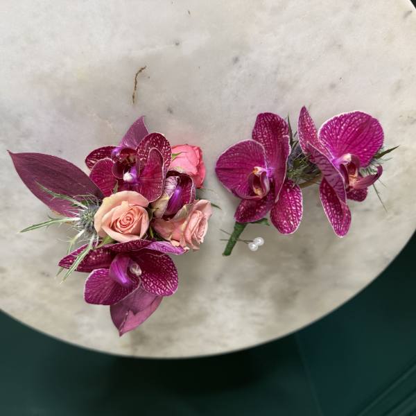 Pair of magenta orchid and peach rose boutonnieres on a round stone surface