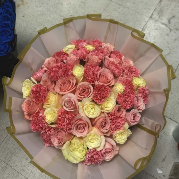 Round bouquet of pink and yellow roses with carnations in pale wrapping