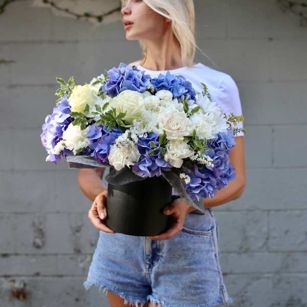 Woman holding a large bouquet of blue and white flowers in a black box