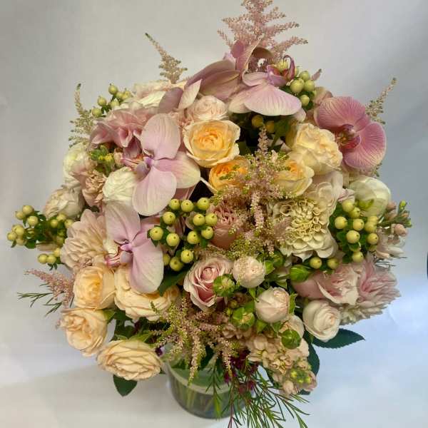 Bouquet of pale pink orchids, cream roses, and green berries in a glass vase