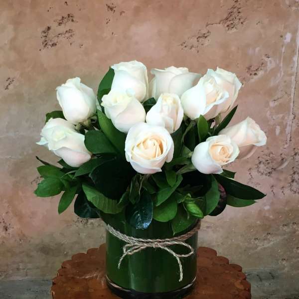 White roses in a green cylindrical vase tied with twine