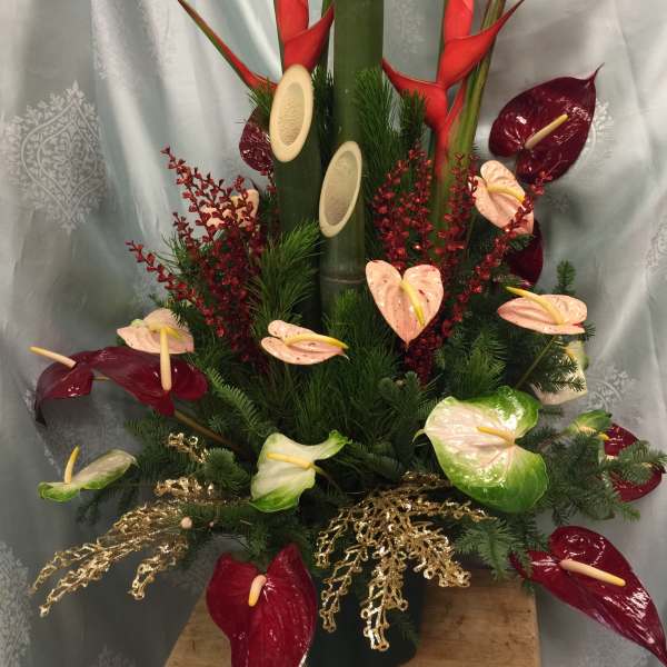 Tropical arrangement with red and pale anthuriums in a tall vase