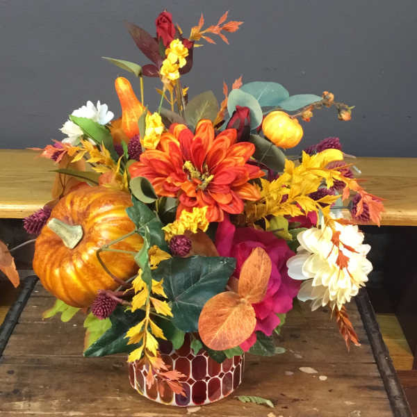 Autumn floral arrangement with pumpkins in a patterned container