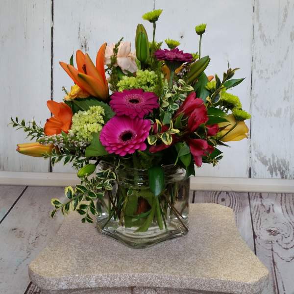 Mixed bouquet of orange lilies, pink gerbera daisies, and green mums in a glass vase