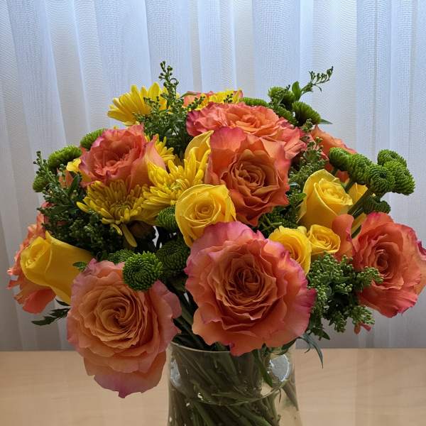 Bouquet of orange and yellow roses with yellow chrysanthemums in a glass vase