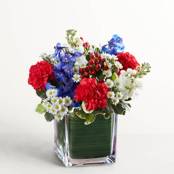 Mixed bouquet of red, blue, and white flowers in a square glass vase