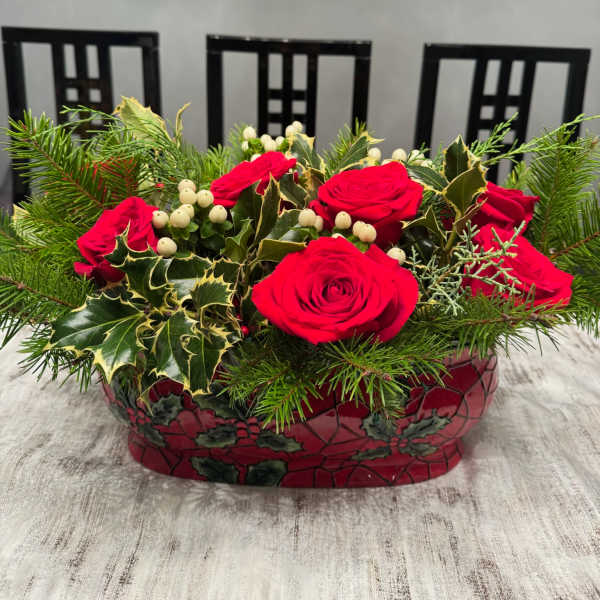 Red roses in a decorative holiday container with evergreen and berry accents
