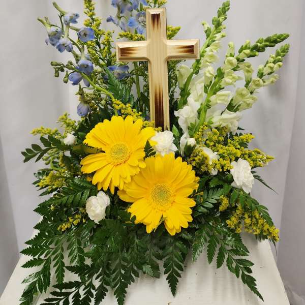 Yellow gerberas and white flowers arranged around a wooden cross