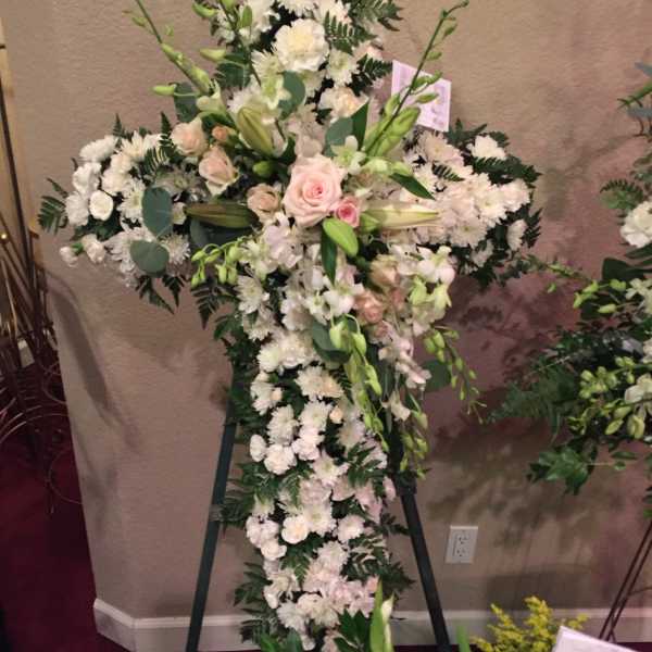 Large white floral cross on an easel with pale pink roses