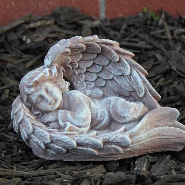 Small sleeping angel figurine with wings, resting on dark mulch