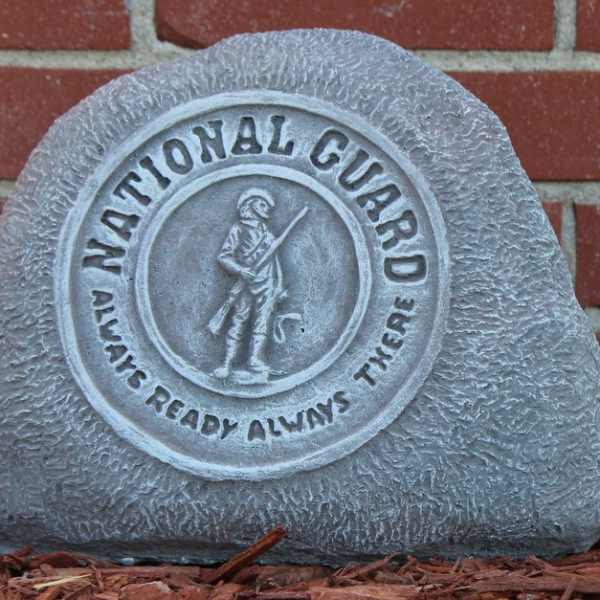 Gray memorial stone with a National Guard emblem against a brick wall
