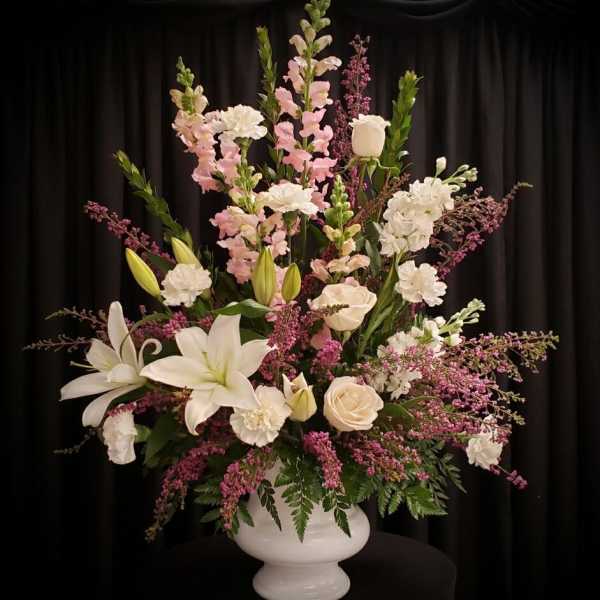 Tall floral arrangement with white lilies, roses, and pink blooms in a white vase
