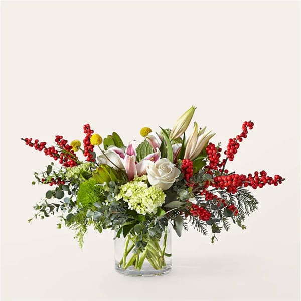 Arrangement of white lilies, roses, and red berry branches in a glass vase