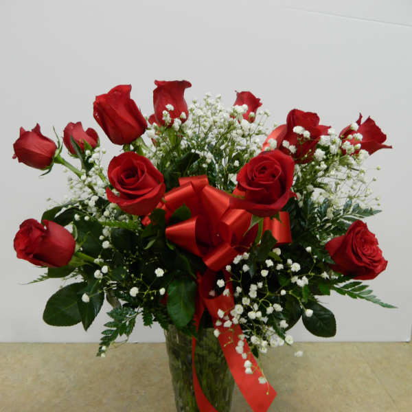 Red roses in a clear glass vase with white baby's breath and a red ribbon