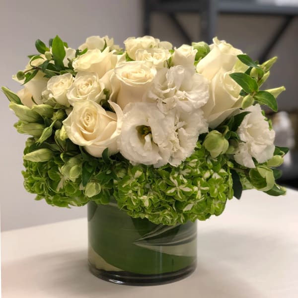 Low arrangement of white roses and lisianthus with green hydrangea in a glass cylinder vase