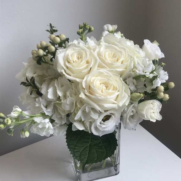 White roses and hydrangeas arranged in a clear square vase