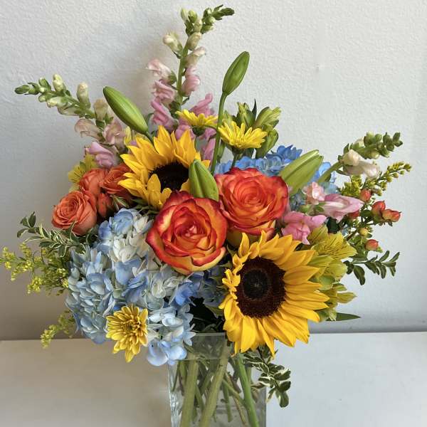 Mixed bouquet with sunflowers, roses, hydrangeas, and snapdragons in a glass vase