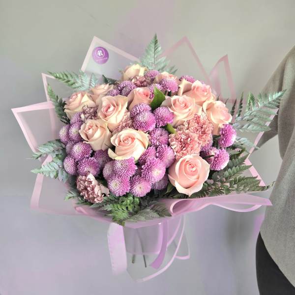 Round bouquet of blush roses, pink carnations, and lavender mums in pink wrapping