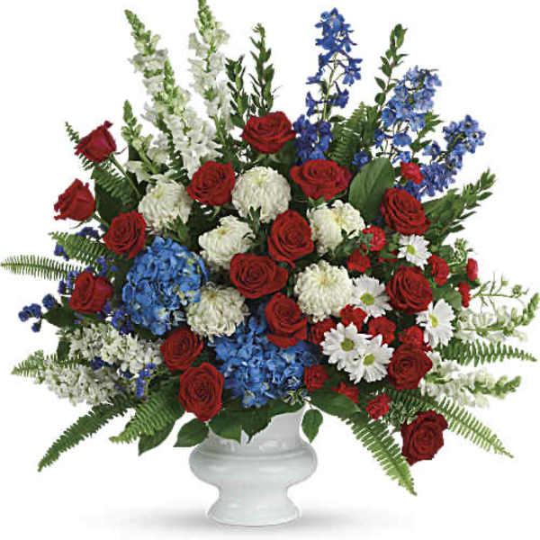 Red roses, blue flowers, and white blooms arranged in a white urn vase