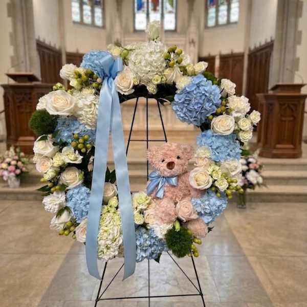 Floral wreath with blue ribbon and teddy bear in a church setting