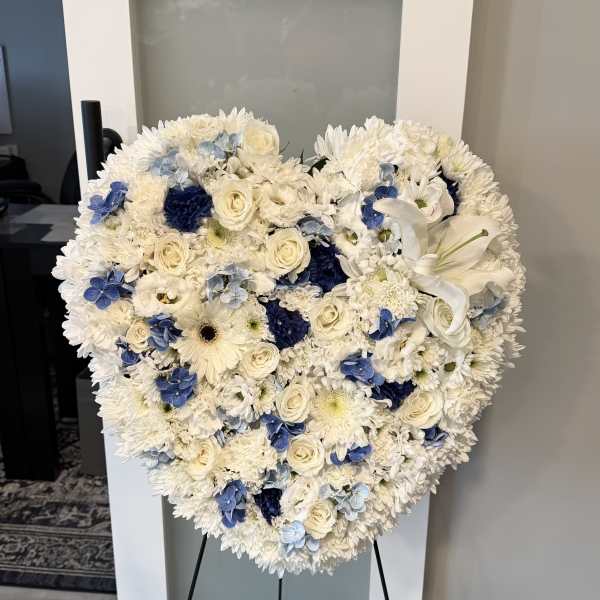 Heart-shaped floral spray with white flowers and blue accents on a stand