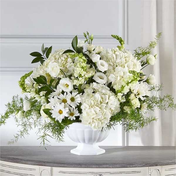 White floral arrangement in a white pedestal vase with green accents