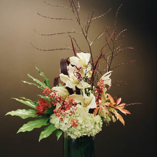 Tall floral arrangement with white orchids and red accents in a green glass vase