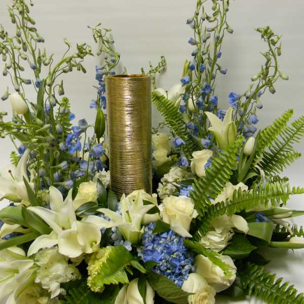 White lilies and blue flowers arranged around a gold cylinder centerpiece