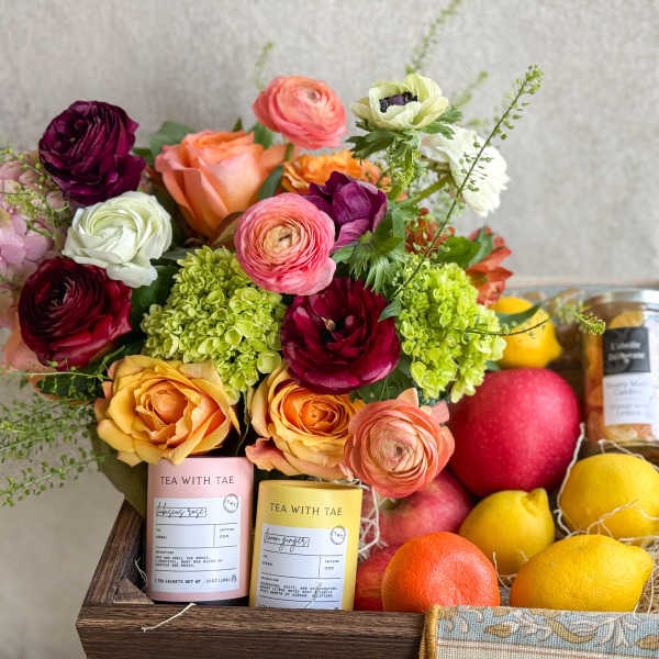 Mixed bouquet with citrus and tea gift items in a wooden crate