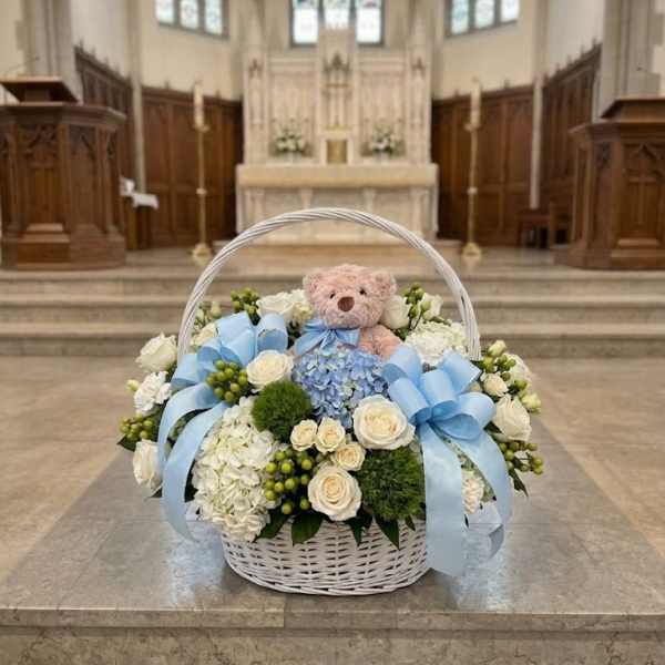 White flower basket with blue ribbons and a teddy bear in a church