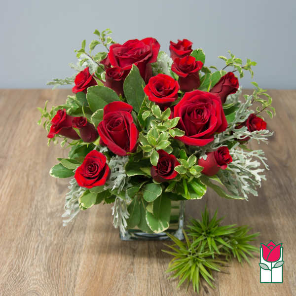 Red roses arranged in a square glass vase with mixed greenery
