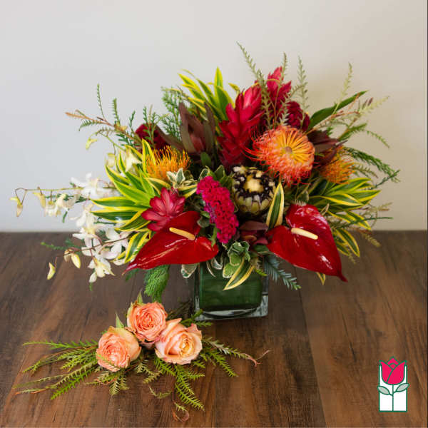 Tropical floral arrangement in a square glass vase with peach roses in front