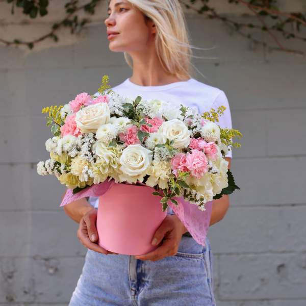 Woman holding a pink hatbox of white and pink flowers