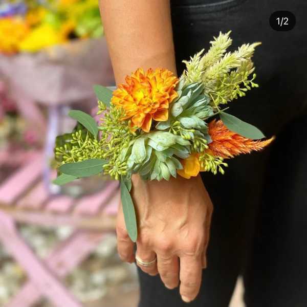 Orange flower wrist corsage with green foliage on a person's wrist