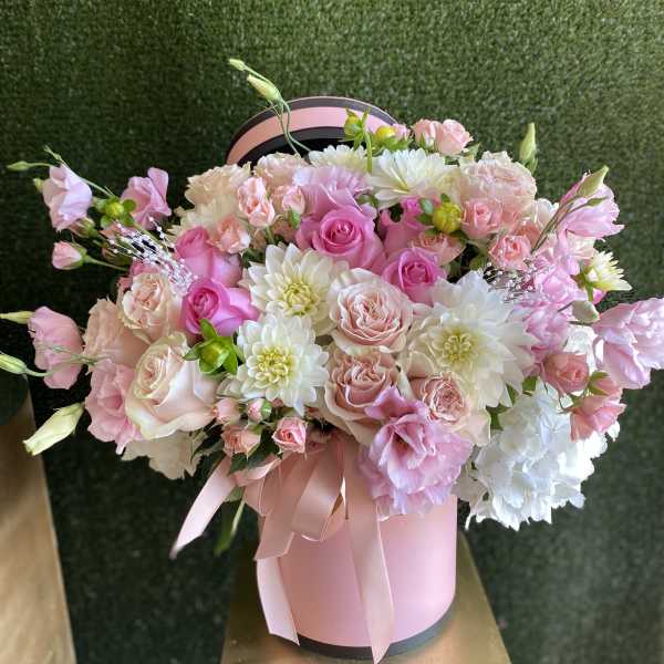 Pink and white flower arrangement with roses in a pink hatbox with ribbon bow