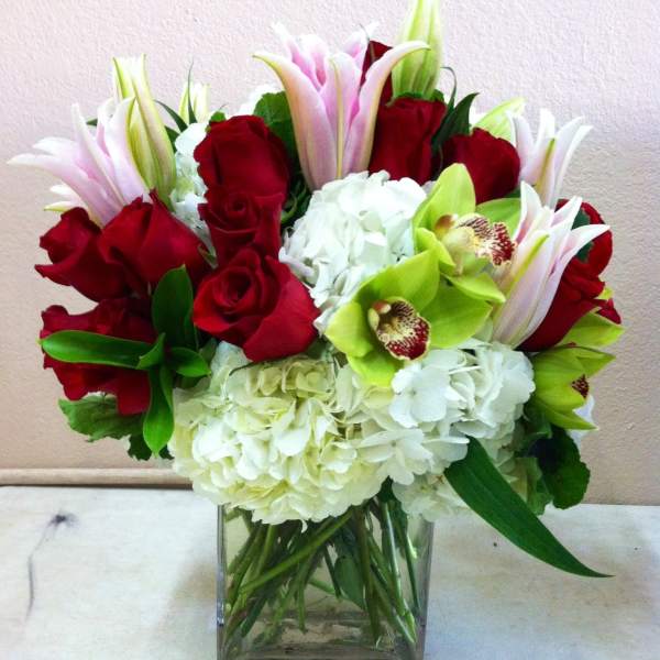 Bouquet of red roses, white hydrangeas, and green orchids in a glass vase