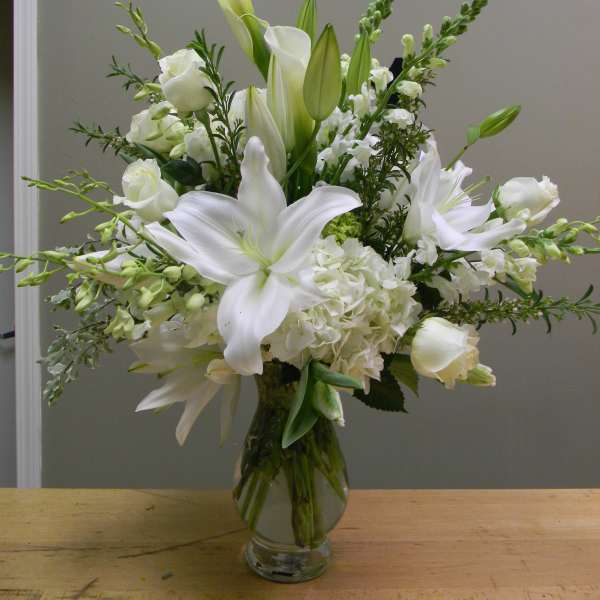 White lilies and roses arranged in a clear glass vase