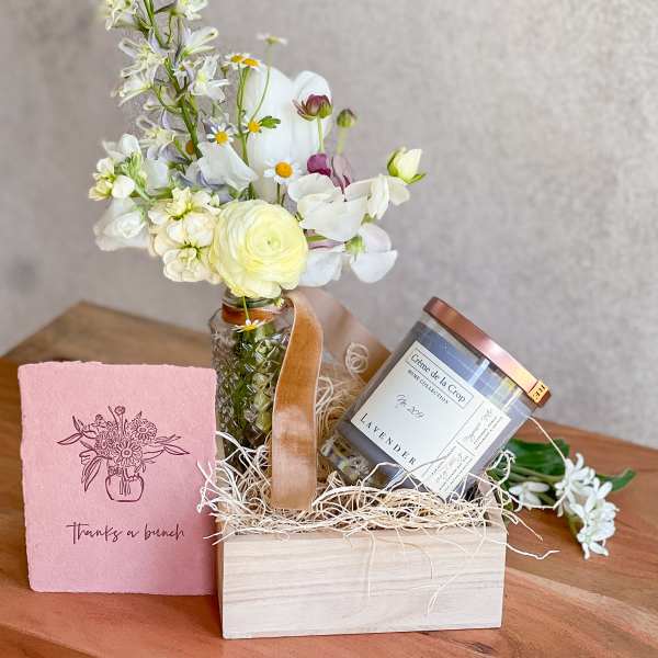 Small flower arrangement in a glass jar with a candle and pink card in a gift box