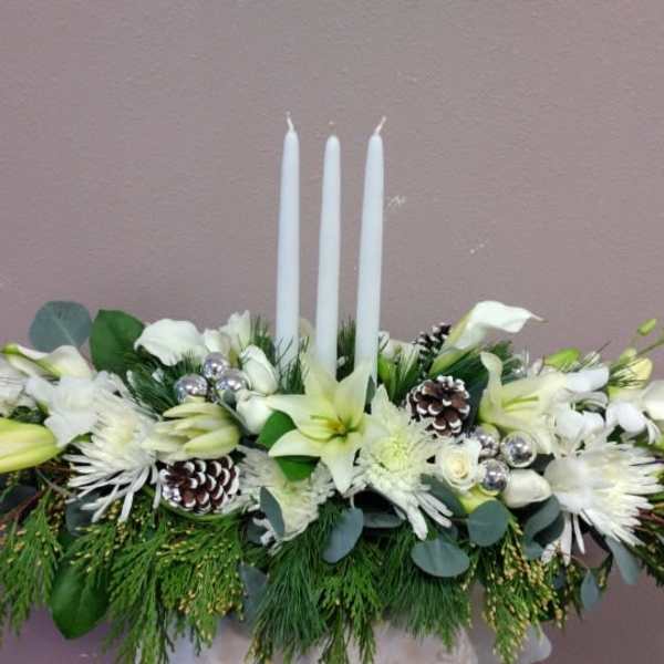 White floral centerpiece with three tall candles and pinecones