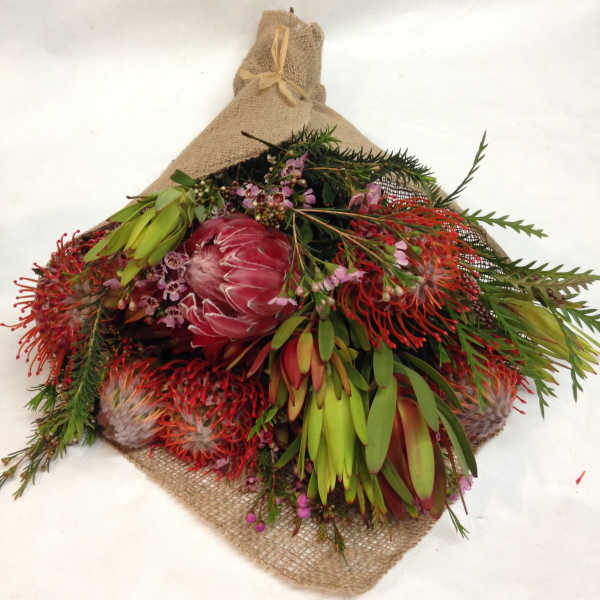 Bouquet of pink protea and red-orange flowers wrapped in burlap
